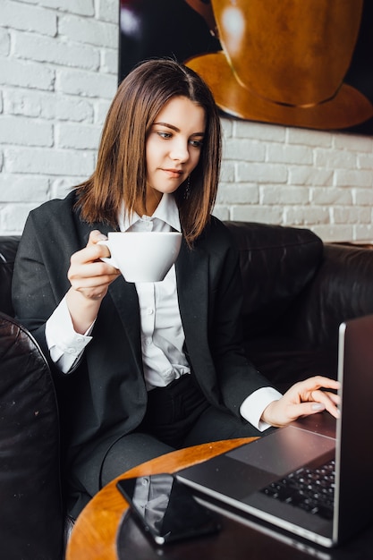 コーヒーとラップトップを持ってカフェに座っている休憩中の女性！