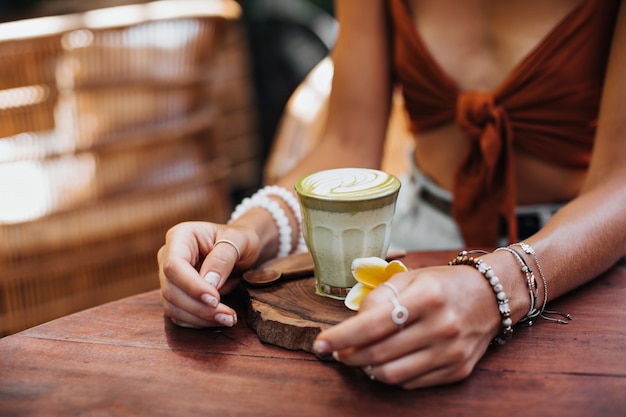 Woman in brown bra sits in cafe and holds glass with matcha latte