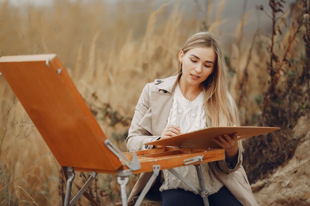 Woman in a brown coat painting in a field