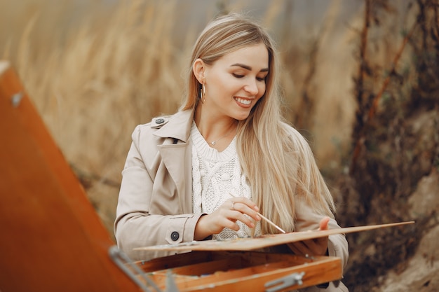 Женщина в коричневом пальто рисует в поле