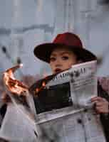 Free photo woman in brown hat holding burning newspaper