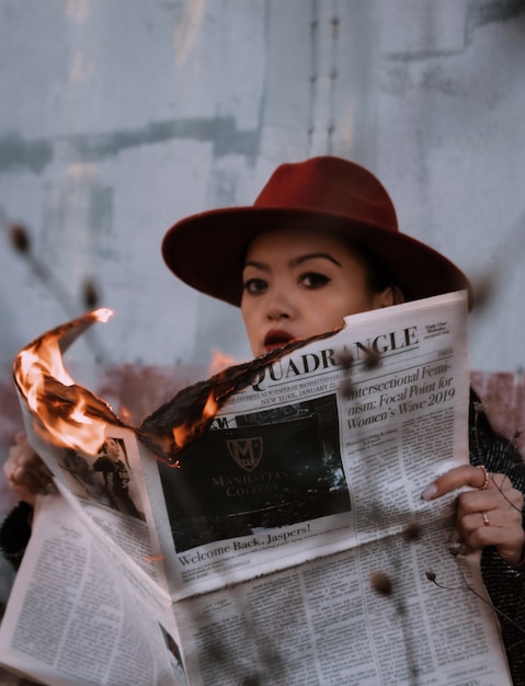 Woman in brown hat holding burning newspaper