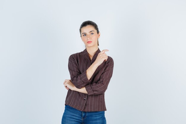 woman in brown striped shirt pointing aside and looking pensive , front view.