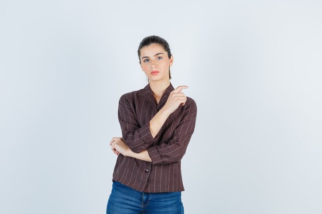 женщина в коричневой полосатой рубашке, указывая в сторону и задумчиво, вид спереди.