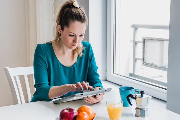 Free photo woman browsing tablet during breakfast