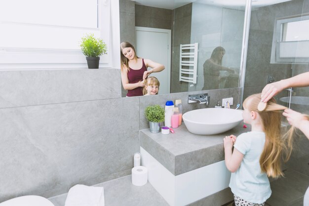 Woman brushing girl near mirror