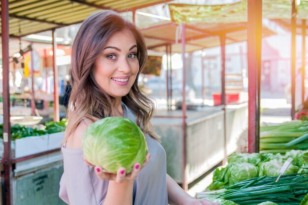 ストリートマーケットで新鮮な有機野菜を買う女性。緑の市場で野菜を買っている若い女性。