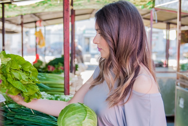 ストリートマーケットで新鮮な有機野菜を買う女性。緑の市場で野菜を買っている若い女性。
