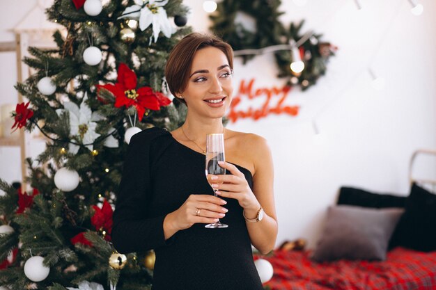 Woman by Christmas tree drinking champaigne