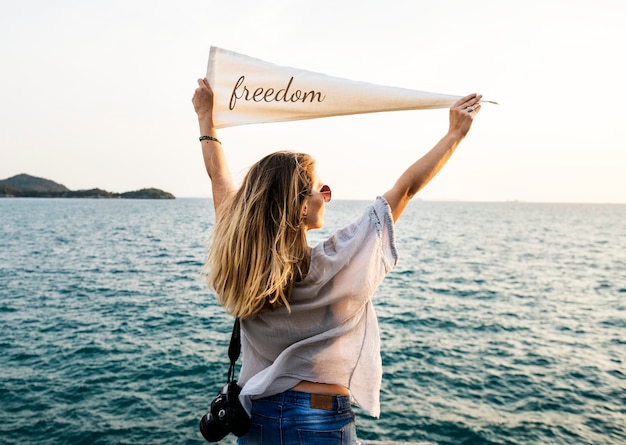 Woman by the sea holding flag with freedom inscription