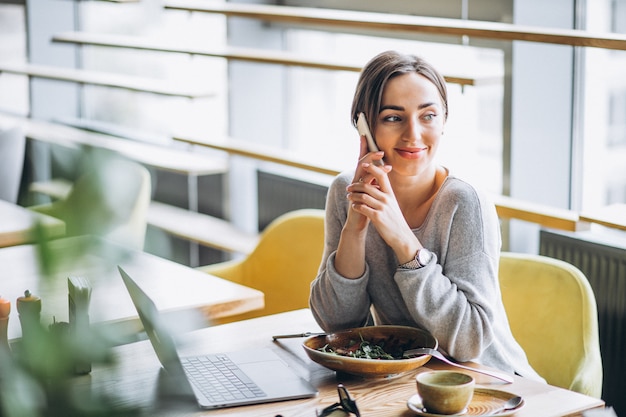 Donna in un caffè pranzando e parlando al telefono