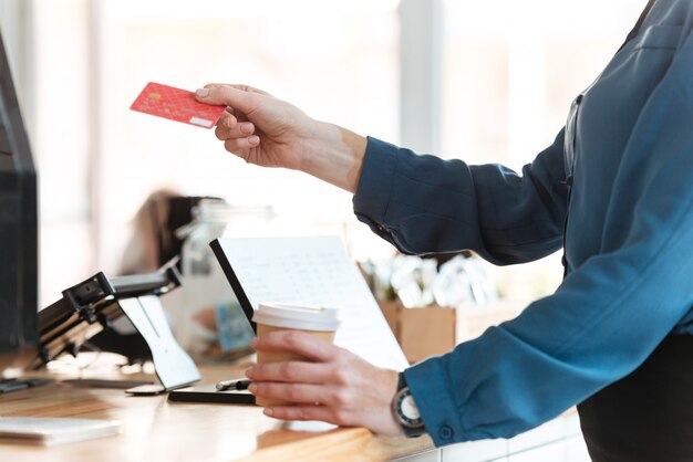 Woman in cafe holding credit card and coffee.