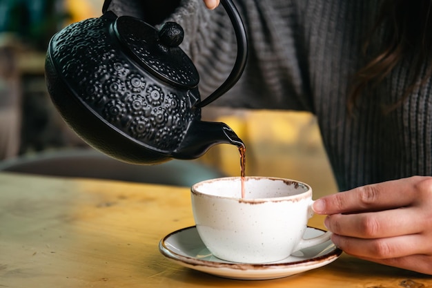 カフェの女性が黒い鋳鉄のティーポットからお茶を注ぐ