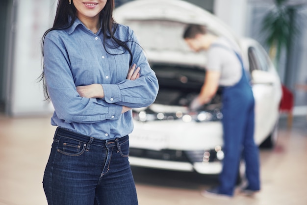 Woman at a car garage getting mechanical service. The mechanic works under the hood of the car