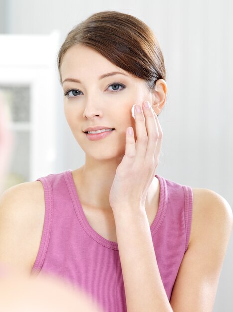 Woman caring of her  beautiful skin on the  face standing near mirror in the bathroom