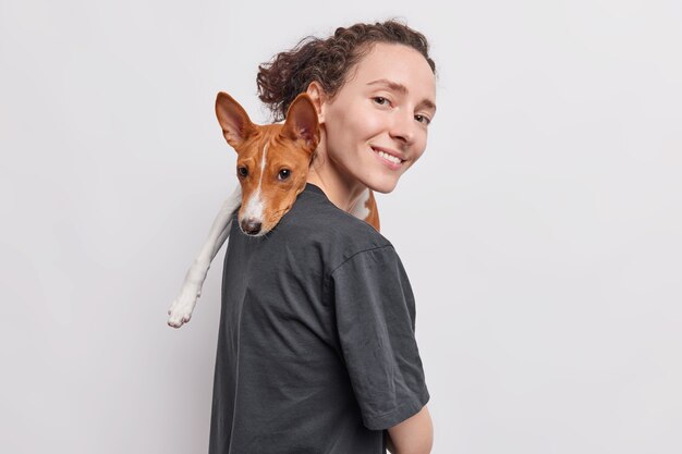 женщина несет собаку на плече, играет с любимым домашним животным, выражает любовь и заботу стоит боком, изолированными на белом