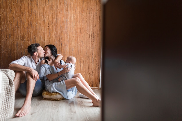 Woman carrying baby kissing her husband sitting on floor