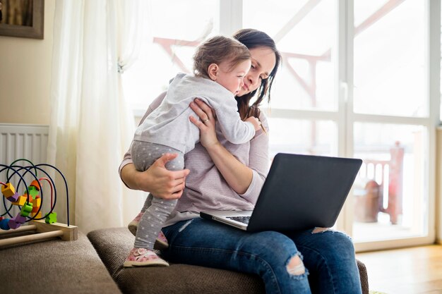 Женщина, несущая дочь, используя ноутбук