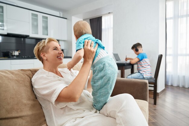 Woman carrying little son while eldest one studying near