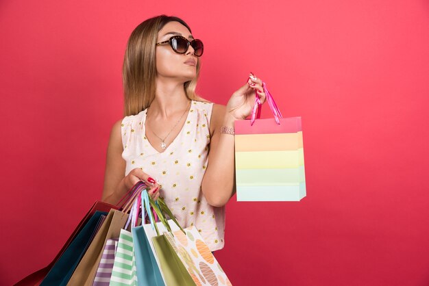 Woman carrying shopping bags on red wall . 