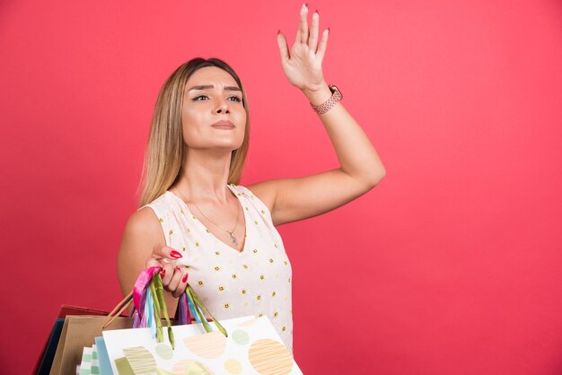 Woman carrying shopping bags while looking up on red wall . 