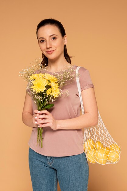 Женщина в повседневной одежде, несущая многоразовую сумку-черепаху и цветы