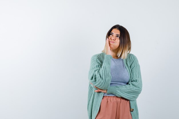 吹き飛ばされた頬に手を保ち、物思いにふける、正面のカジュアルな服装の女性。