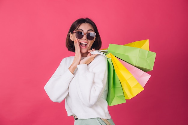 Woman in casual white sweater and sunglasses on red wall