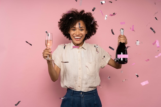 Woman celebrating with champagne glass and bottle amongst confetti