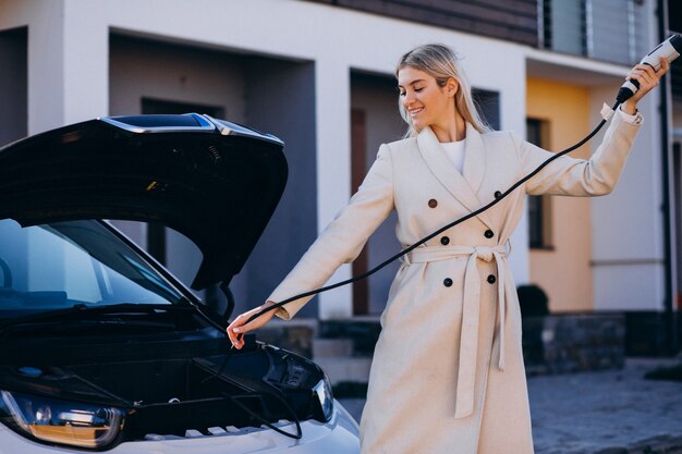 Woman charging electro car by her house and holding charger