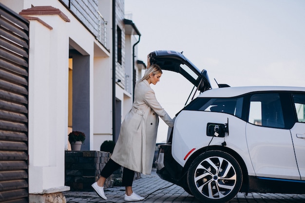 Женщина заряжает электро автомобиль возле своего дома