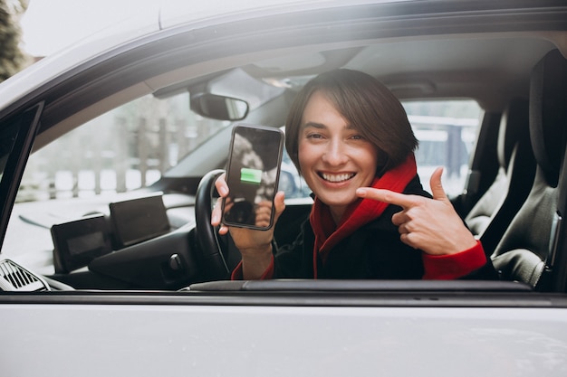 Woman charging her car and looking at the cherger on bher phone