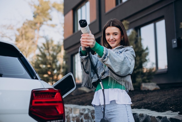 Женщина заряжает свой электромобиль зарядным пистолетом