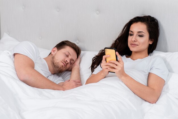 Woman checking her phone next to asleep boyfriend