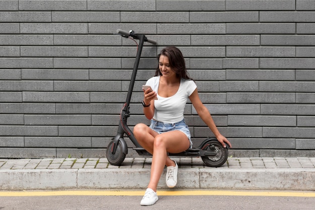 Foto gratuita donna che controlla il suo telefono mentre è seduto su uno scooter