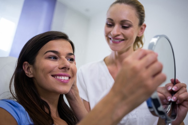 Женщина проверяет свою кожу в зеркале после получения косметического лечения