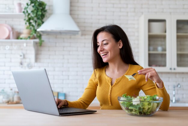 ラップトップをチェックし、サラダを食べる女