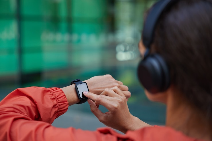 Free Photo  woman checks results of fitness training on smartwatch listens music via headphones dressed in anorak poses on blurred 