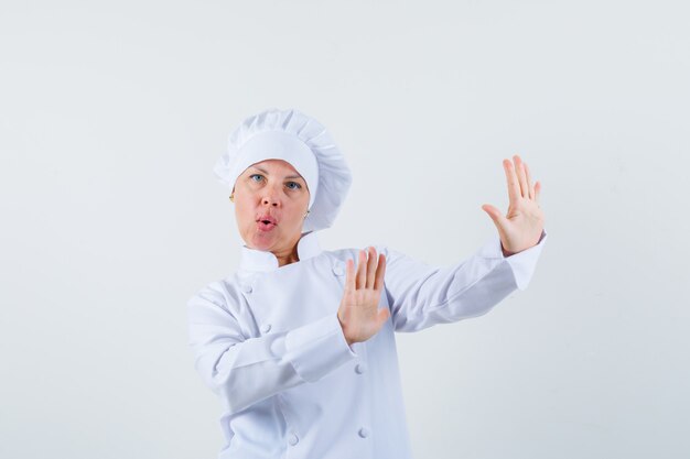 흰색 유니폼을 입고 자신을 방어하고 불안해 보이는 여자 요리사