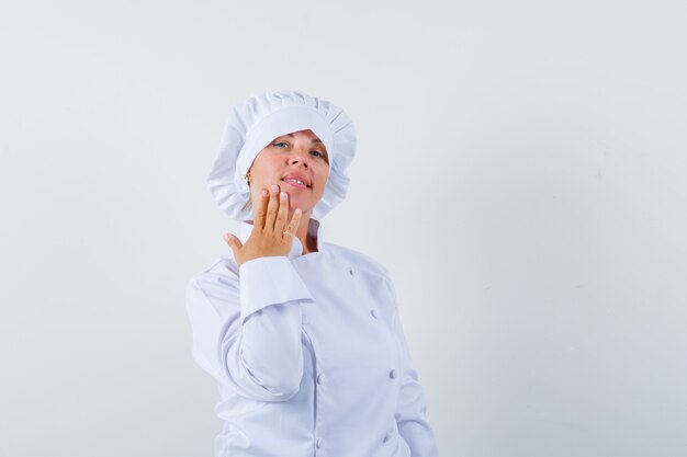 woman chef holding fingers on chin in white uniform and looking delicate.