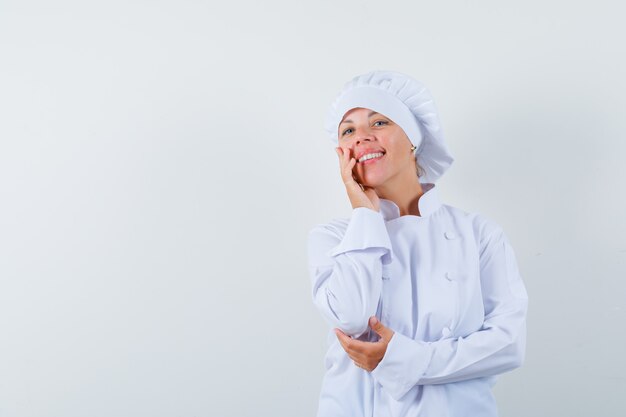 woman chef holding hand on cheek in white uniform and looking elegant