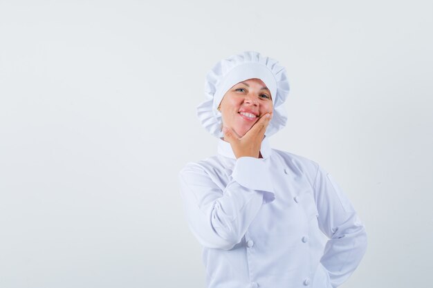 woman chef holding hand on chin in white uniform and looking glad