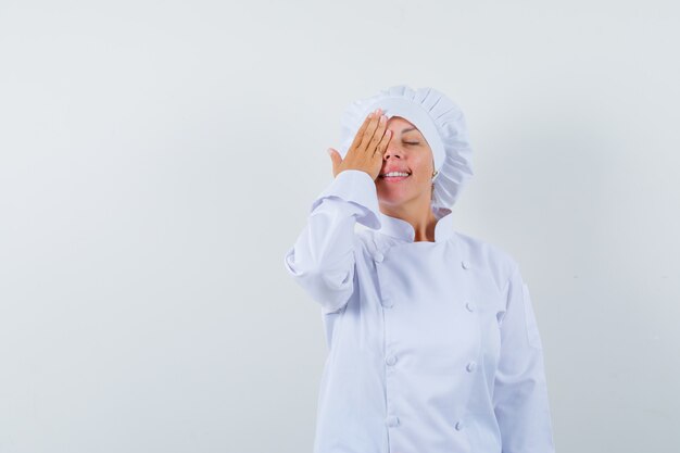 женщина-повар держит руку на глазу в белой форме и выглядит мирно