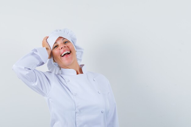 женщина-повар держит руку на голове в белой форме и выглядит веселым.