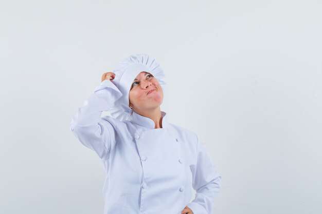 흰색 유니폼을 입고 머리에 손을 잡고 주저하는 여자 요리사