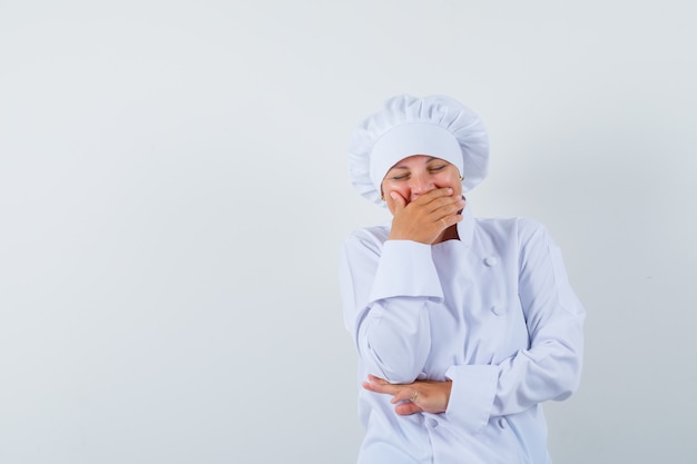 woman chef holding hand on mouth in white uniform and looking joyous