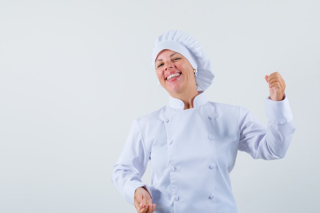Женщина-повар в белой форме позирует, как держит что-то и выглядит весело
