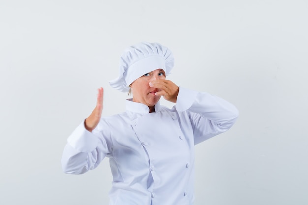 woman chef pinching nose due to bad smell in white uniform and looking disgusted