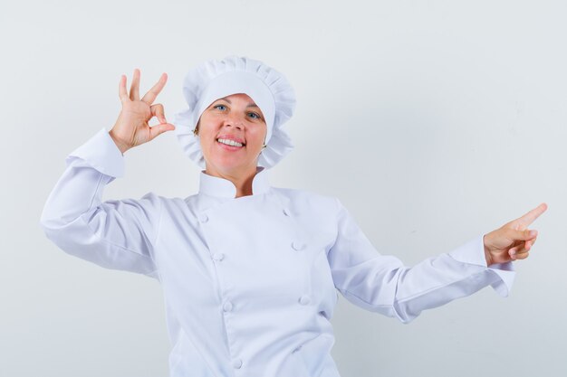 여자 요리사 옆으로 가리키는, 흰색 유니폼에 확인 제스처를 보여주는 자신감을 찾고.