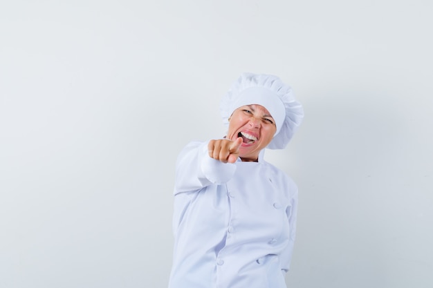 woman chef pointing at front in white uniform and looking happy.